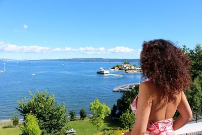 Rear view of woman standing by sea against blue sky