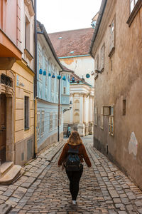 Rear view of woman walking on footpath amidst buildings