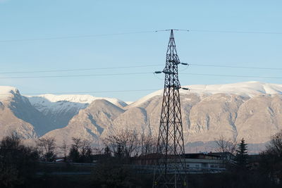 Electricity pylon on snow covered landscape against clear sky