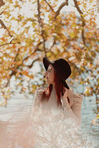 Woman looking away while standing on tree during autumn