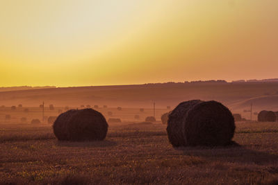 Hay bales on field against sky during sunset