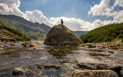 A tourist sitting on a rock in a middle of a stream river in high tatra in the valley of five lakes