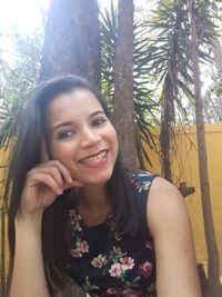 Portrait of smiling young woman against tree trunk