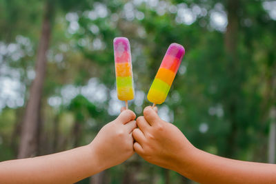 Cropped hands of people holding popsicles against trees