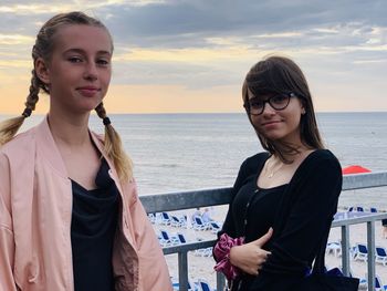 Portrait of smiling sisters standing against sea at sunset