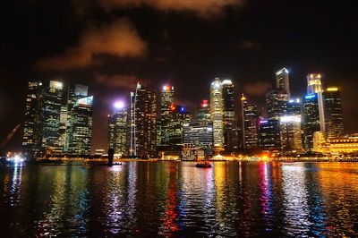 Illuminated buildings by river against sky at night