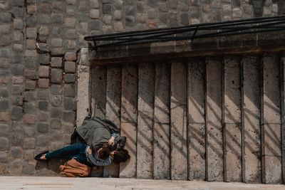 Full length of man sitting on wall against building