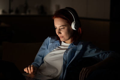 Concentrated middle aged programmer female sits on chair work on laptop at night. freelancr concept