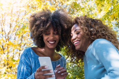 Two female afro american friends checking social media holding smartphone outdoors.
