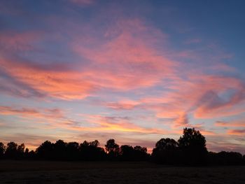 Silhouette trees on field against romantic sky at sunset