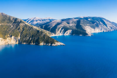 Scenic view of sea and mountains against clear blue sky