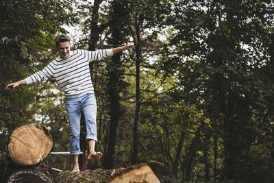 Cheerful mature man walking on log in forest