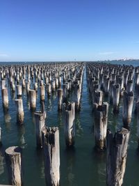 Wooden posts in sea against clear blue sky