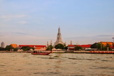 Boats in river by buildings against sky