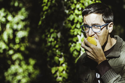 Close-up portrait of young man eating fruit while standing against plants