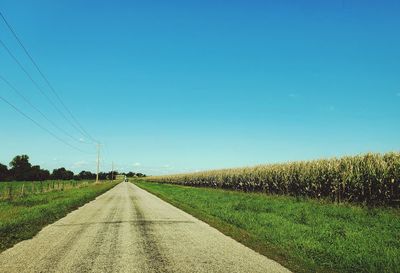 Road amidst field against clear blue sky