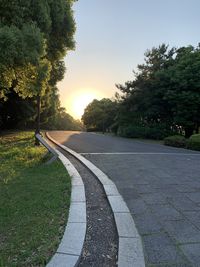 Footpath by road against sky during sunset