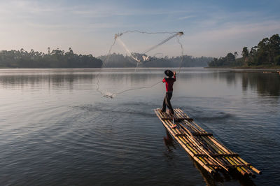 Man fishing in lake against sky