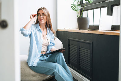 Young woman in bue shirt with notes in hands sitting on chair in room