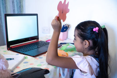 Rear view of girl using laptop on table