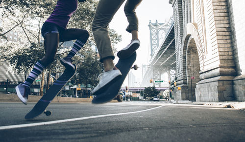 Low section of people skateboarding on road against building