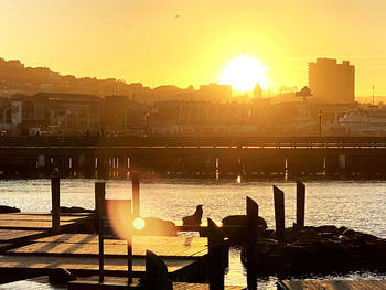 Silhouette people sitting on river by cityscape against sky during sunset