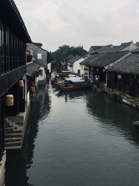 Boats moored on canal amidst houses against sky