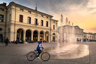 Man riding bicycle on building in city against sky