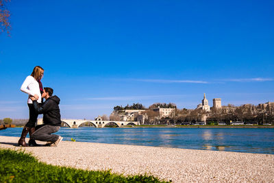 Couple at riverbank against clear blue sky