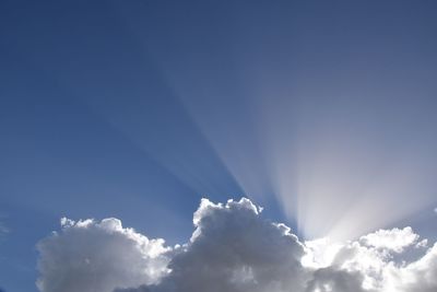 Low angle view of sunlight streaming through clouds