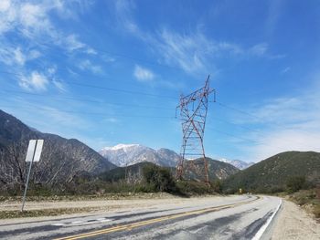 Electricity pylon by mountain against sky