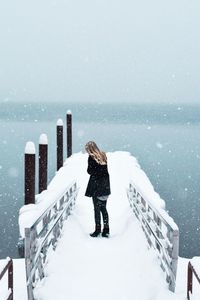 Woman standing on snow covered railing against clear sky