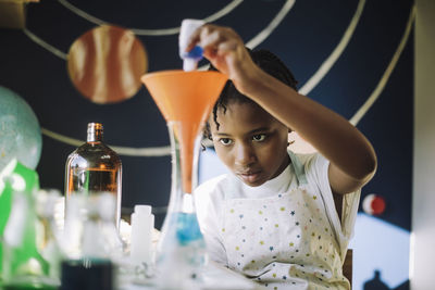 Ambitious girl mixing chemical solution while learning science project at table