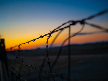 Close-up of silhouette barbed wire fence against sky during sunset