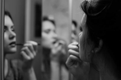 Close-up of woman applying make-up against mirror