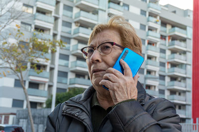 Portrait of a senior woman talking with a modern smartphone in the city streets.