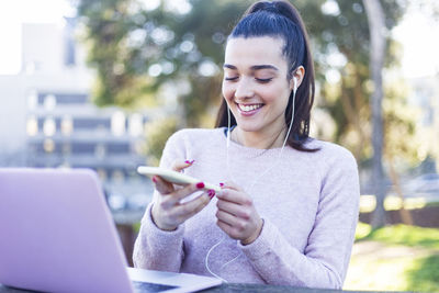 Smiling young woman using mobile phone while sitting outdoors