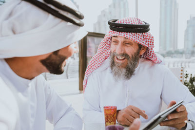 Men wearing dish dash discussing over digital tablet outdoors