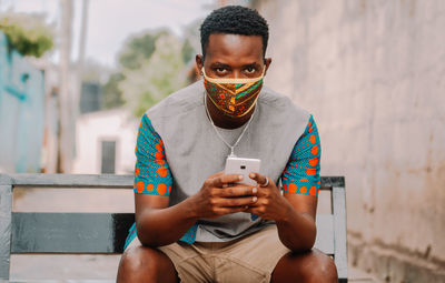 Portrait of young man using mobile phone while sitting against wall