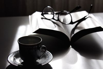 Coffee cup with eyeglasses on open book at table