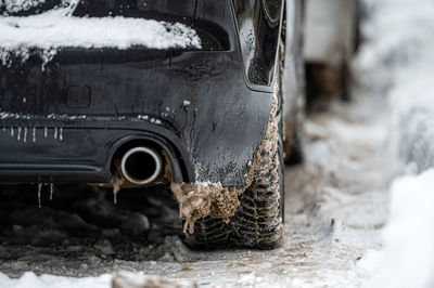 Close-up rear view of a dark car on parking, dirty rear wheel tire on snow