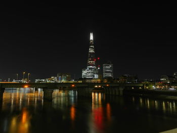 Illuminated buildings by river against sky at night