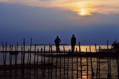Silhouette men standing by sea against sky during sunset