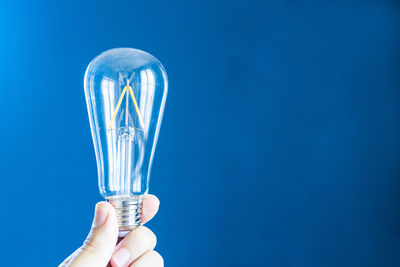 Close-up of hand holding light bulb against blue background