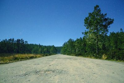 Road amidst trees against clear blue sky