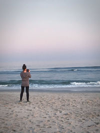 A girl stands photographing the sunset at the beach
