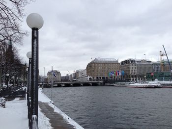 View of buildings by river against cloudy sky