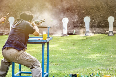 Rear view of man aiming with gun while standing in park