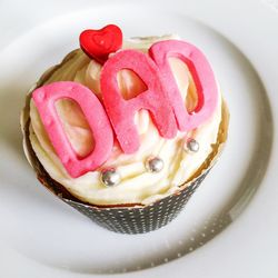 High angle view of pink dad text with red heart icing on cupcake in plate