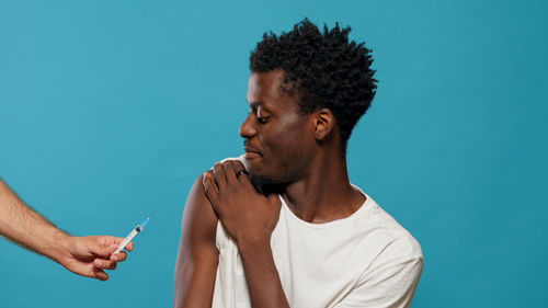 Man taking vaccine while sitting against blue background